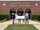 Five people stand in front of a brick building labeled “Lafayette County School Auditorium.” The group is holding an oversized check with the ExxonMobil logo, made out to the Lafayette County School District for $10,000.