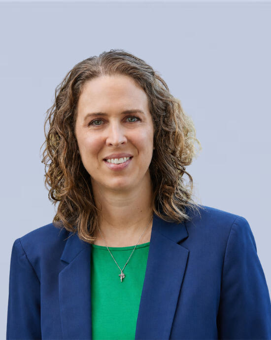 Carolyn Fenn with shoulder-length curly hair is shown in a professional headshot against a plain light gray background.
