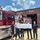 Five people stand in front of the Stamps Fire Department, posing with a large symbolic check. The check shows ExxonMobil as the donor and is made out to the Stamps Rural Fire District for $10,00