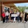 A group of ten people stands in a line outside a brick building, posing for a photo under a covered walkway. Several are dressed in business or business-casual attire, and two people in the center hold a large ceremonial check with the ExxonMobil logo.