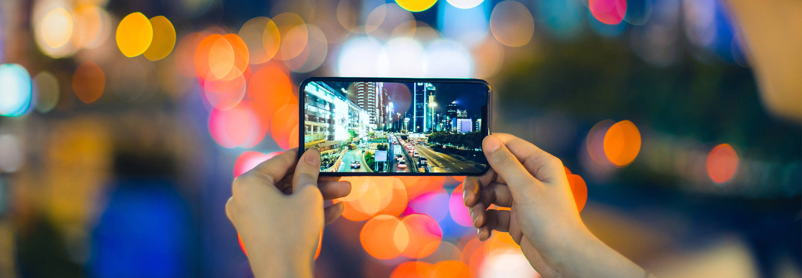 Woman taking a picture of city lights at night with her phone. 